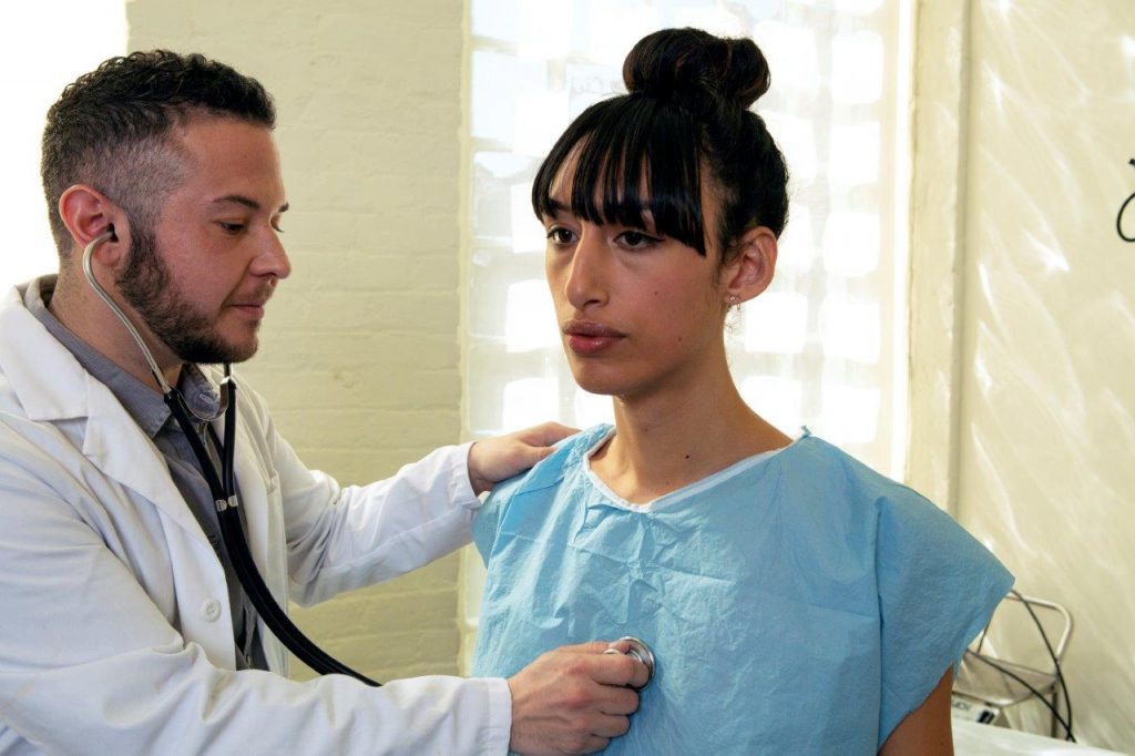 A transgender woman in a hospital gown being treated by a doctor a